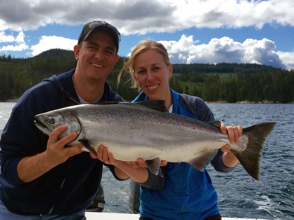 A smiling man and woman holding a salmon.