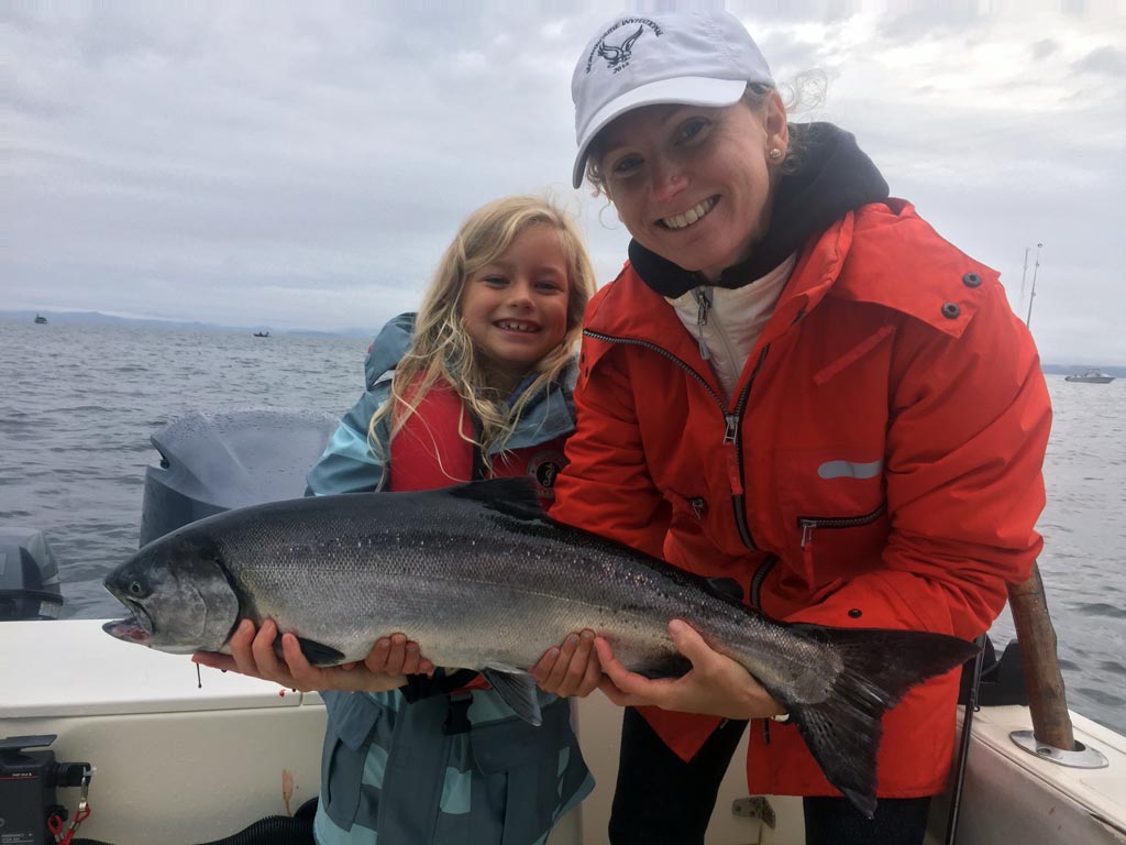 A lady and a girl both smiling and holding a salmon.